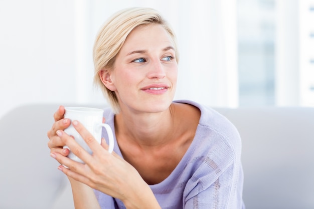 Mujer bonita rubia relajante en el sofá y sosteniendo una taza