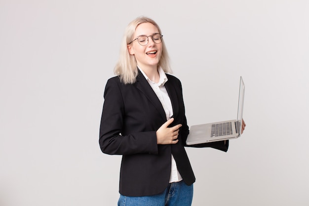 Mujer bonita rubia riendo a carcajadas de una broma hilarante y sosteniendo una computadora portátil