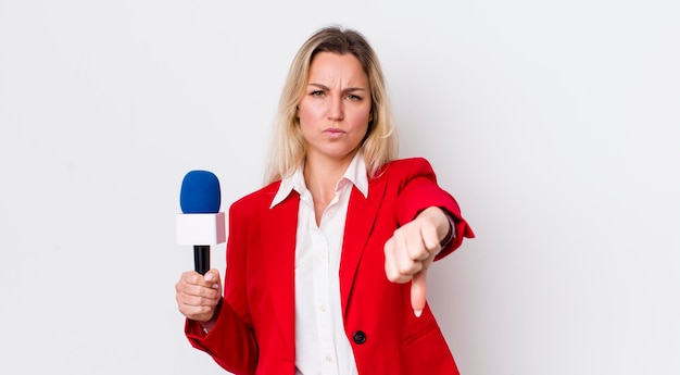 Mujer bonita rubia sintiéndose mostrando los pulgares hacia abajo concepto de preportador y micrófono