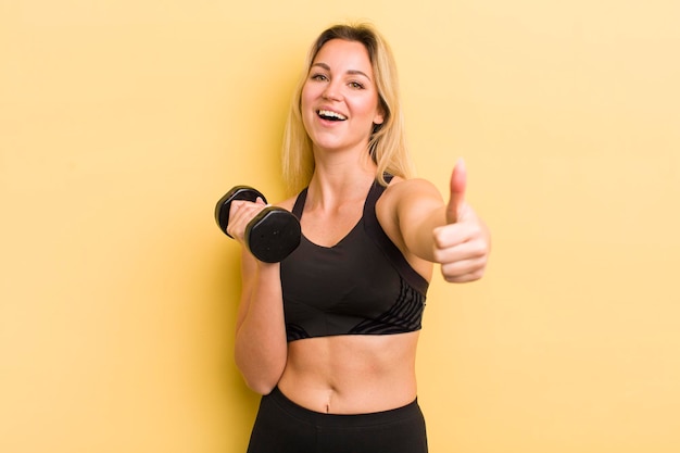 Mujer bonita rubia sintiéndose orgullosa sonriendo positivamente con los pulgares hacia arriba