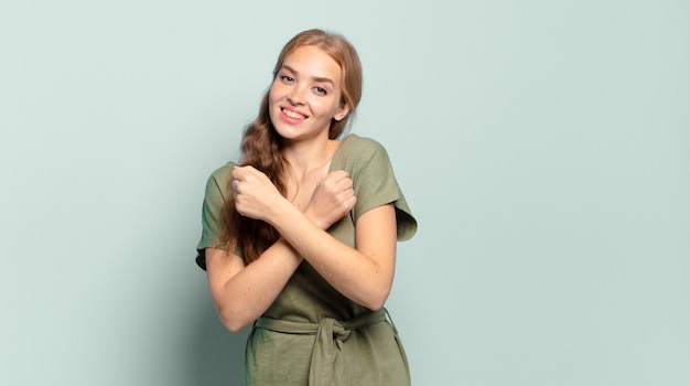 Mujer bonita rubia sonriendo alegremente y celebrando, con los puños apretados y los brazos cruzados, sintiéndose feliz y positivo