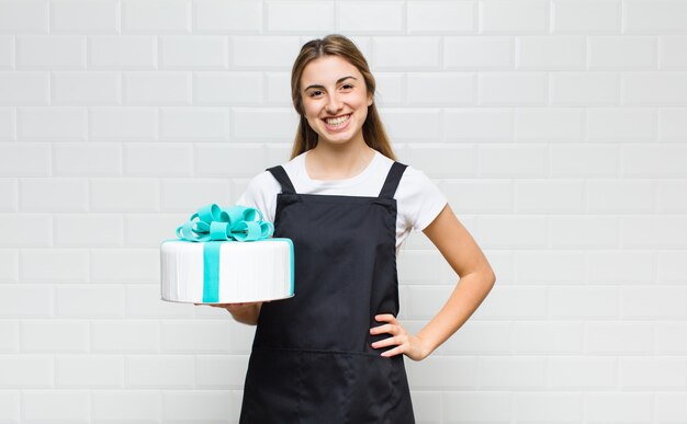 Mujer bonita rubia sonriendo felizmente con una mano en la cadera y actitud confiada, positiva, orgullosa y amistosa