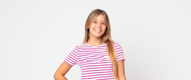 Mujer bonita rubia sonriendo felizmente con una mano en la cadera y actitud confiada, positiva, orgullosa y amistosa