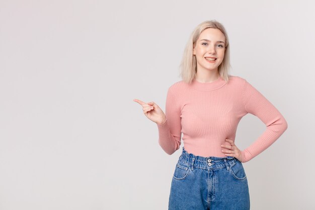 Mujer bonita rubia sonriendo felizmente con una mano en la cadera y confiada