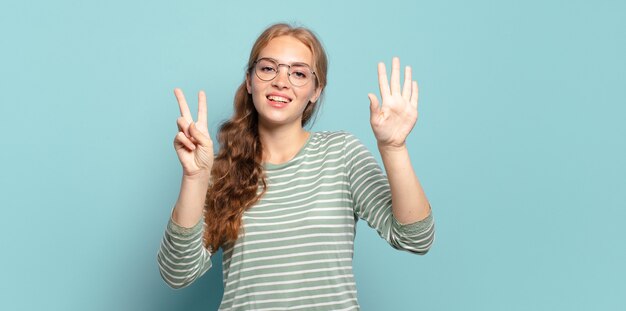 Mujer bonita rubia sonriendo y mirando amistosamente, mostrando el número siete o séptimo con la mano hacia adelante, contando hacia atrás