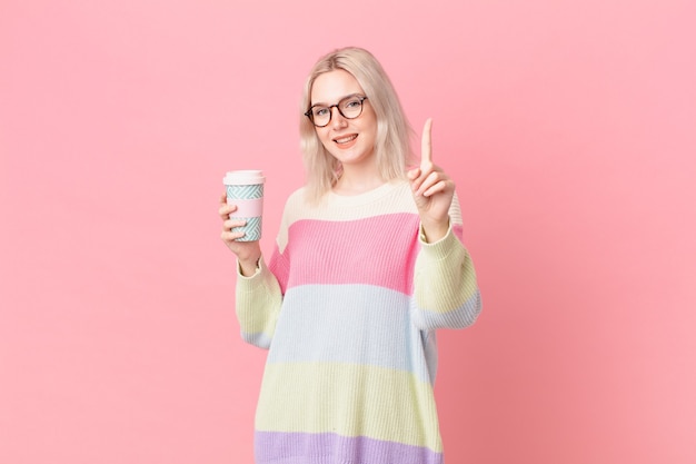 Mujer bonita rubia sonriendo con orgullo y confianza haciendo el número uno. concepto de cafe