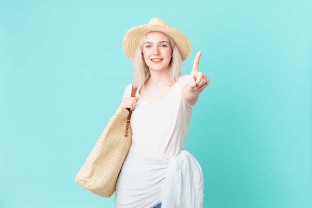 Mujer bonita rubia sonriendo con orgullo y confianza haciendo el número uno. concepto de verano