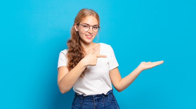 Mujer bonita rubia sonriendo, sintiéndose feliz, despreocupada y satisfecha, señalando el concepto o la idea en el espacio de la copia en el lateral