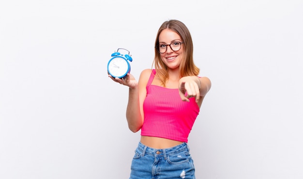 Mujer bonita rubia sosteniendo un reloj despertador y señalando