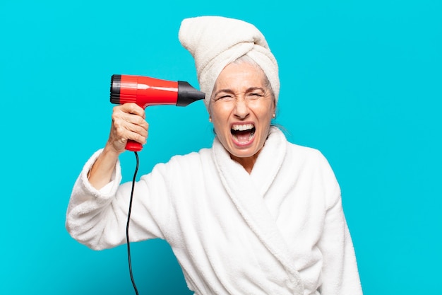 Mujer bonita senior después de la ducha con albornoz. concepto de secador de pelo