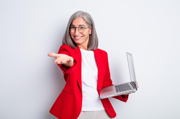 Mujer bonita senior sonriendo felizmente con amabilidad y ofreciendo y mostrando un concepto. concepto de negocio y portátil