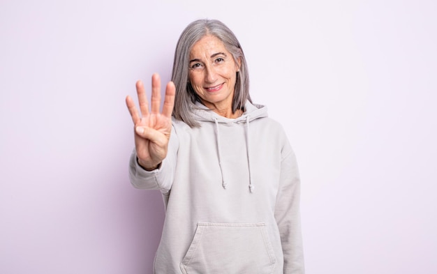 mujer bonita senior sonriendo y luciendo amigable, mostrando el número cuatro o cuarto con la mano hacia adelante, contando hacia atrás