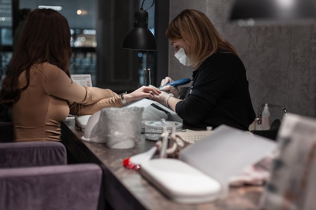 Mujer bonita se sienta y hace una manicura en el estudio de belleza Mujer manicurista profesional trabaja en estudio y hace uñas