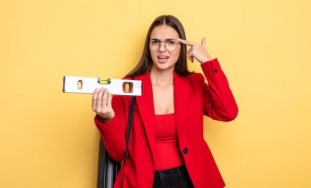 mujer bonita sintiéndose confundida y perpleja, mostrando que estás loco. arquitecto con un nivel