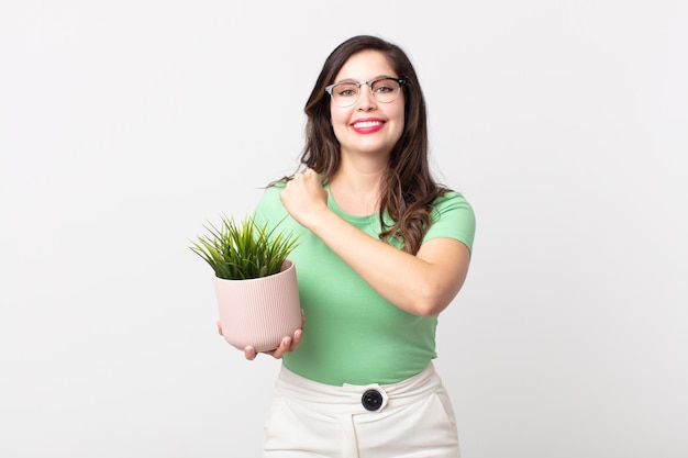 Mujer bonita sintiéndose feliz y enfrentando un desafío o celebrando y sosteniendo una planta decorativa