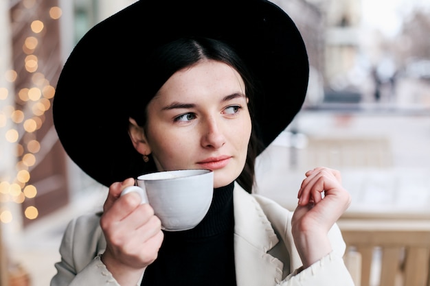 Mujer bonita en sombrero negro fedora hipster disfrutando de café en una cafetería.