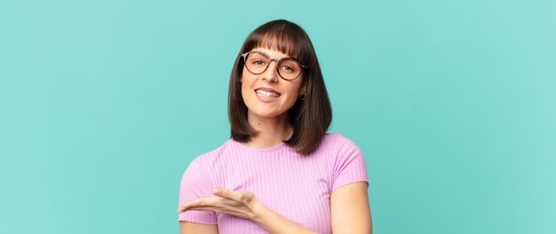 Mujer bonita sonriendo alegremente, sintiéndose feliz y mostrando un concepto en el espacio de la copia con la palma de la mano