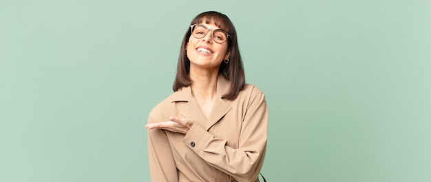 Mujer bonita sonriendo alegremente, sintiéndose feliz y mostrando un concepto en el espacio de la copia con la palma de la mano