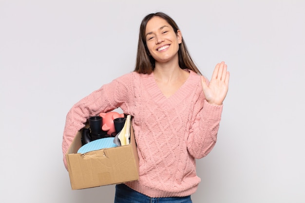 Foto mujer bonita sonriendo feliz y alegremente, saludando con la mano, dándote la bienvenida y saludándote, o despidiéndote