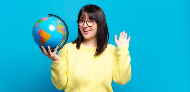 Foto mujer bonita sonriendo feliz y alegremente, saludando con la mano, dándote la bienvenida y saludándote, o despidiéndote