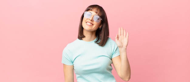 Mujer bonita sonriendo feliz y alegremente, saludando con la mano, dándote la bienvenida y saludándote, o diciéndote adiós