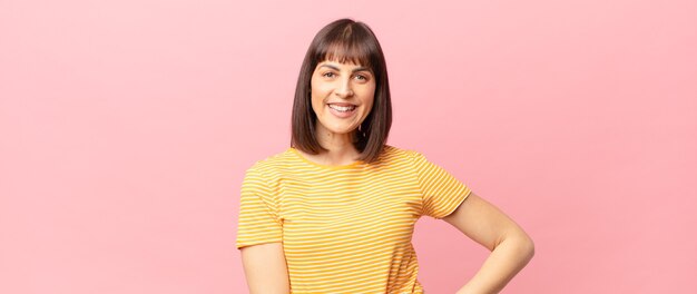 Mujer bonita sonriendo felizmente con una mano en la cadera y actitud confiada, positiva, orgullosa y amistosa