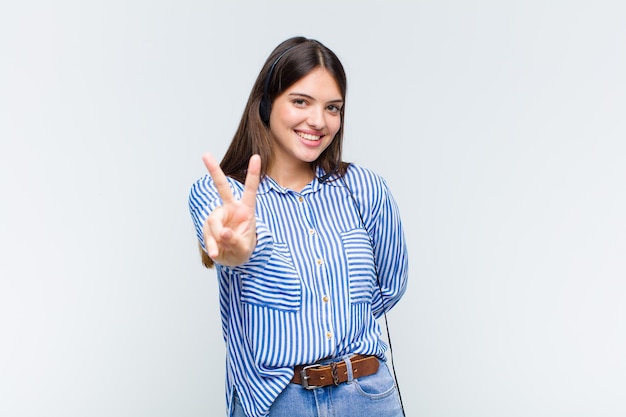 Mujer bonita sonriendo y luciendo feliz, despreocupada y positiva, gesticulando victoria o paz con una mano