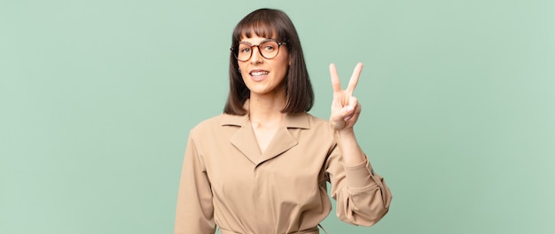 Mujer bonita sonriendo y luciendo feliz, despreocupada y positiva, gesticulando victoria o paz con una mano