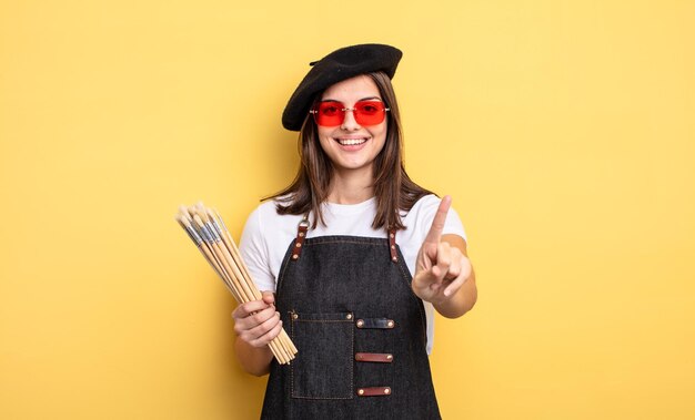 Mujer bonita sonriendo con orgullo y confianza haciendo el concepto de artista pintor número uno