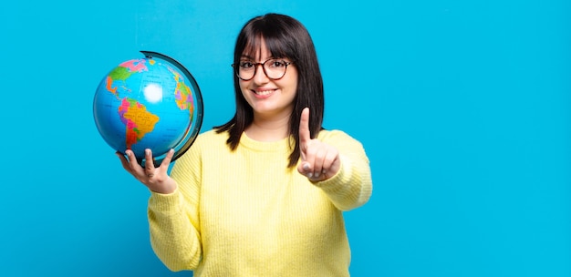 Mujer bonita sonriendo con orgullo y confianza haciendo la pose número uno triunfalmente, sintiéndose como una líder