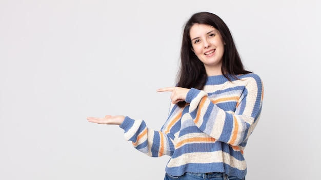 Mujer bonita sonriendo, sintiéndose feliz, despreocupada y satisfecha, señalando el concepto o la idea en el espacio de la copia en el lateral