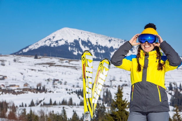 Mujer bonita sonriente joven que sostiene el esquí. montañas en el fondo. viajes de invierno. copia espacio