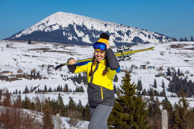 Mujer bonita sonriente joven que sostiene el esquí. montañas en el fondo. viajes de invierno