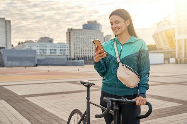 Mujer bonita sonriente mirando la pantalla del teléfono inteligente al aire libre