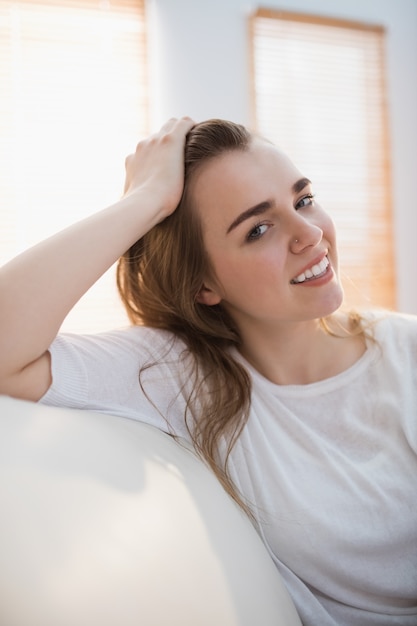 Mujer bonita sonriente que sostiene su pelo en el sofá en la sala de estar