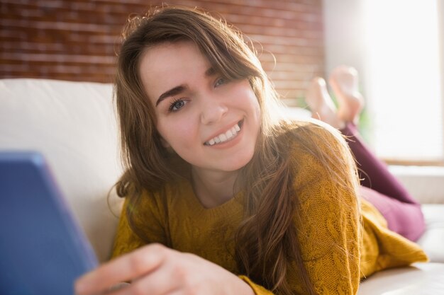 Mujer bonita sonriente que usa la tableta en el sofá en la sala de estar