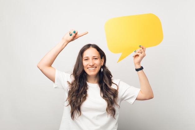 Una mujer bonita sonriente sostiene un discurso de burbuja amarillo y lo señala.