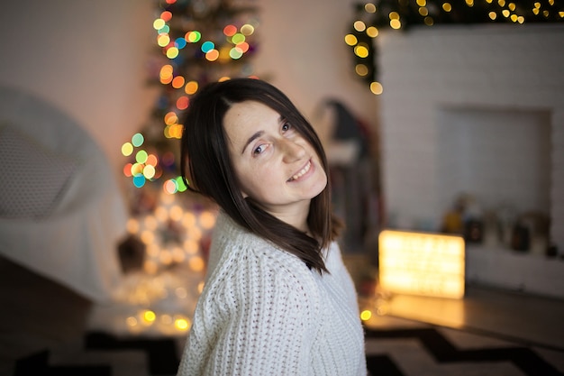 Una mujer bonita en suéter blanco sonriendo y delante del árbol de Navidad.