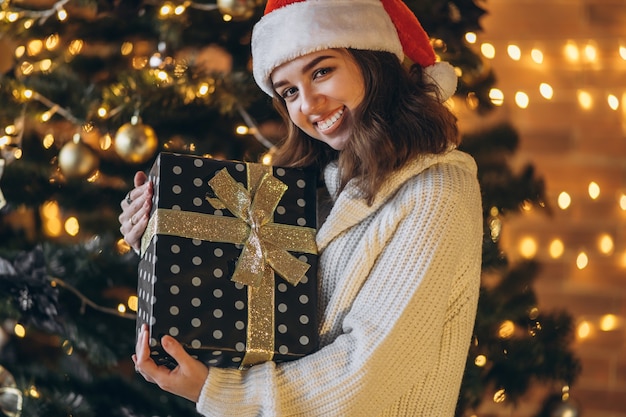 Mujer bonita en suéter cálido y gorro de Navidad, sosteniendo caja de regalo