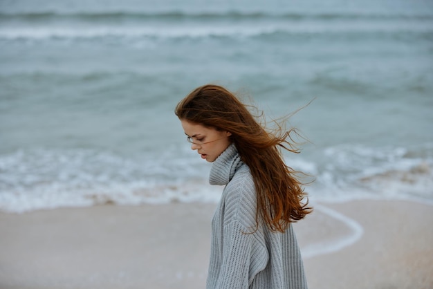 Mujer bonita en un suéter que vuela el pelo por el turismo oceánico inalterado