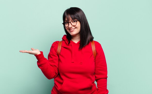 Mujer bonita de talla grande sonriendo alegremente, sintiéndose feliz y mostrando un concepto en el espacio de la copia con la palma de la mano