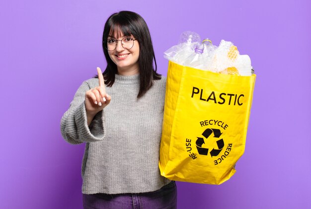 Mujer bonita de talla grande sonriendo con orgullo y confianza haciendo la pose número uno triunfalmente, sintiéndose como una líder