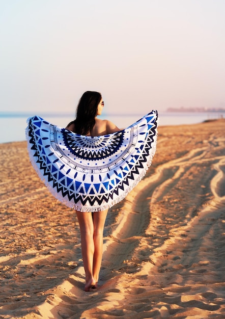 Mujer bonita con un tapiz de playa redondo mandala en la costa del océano