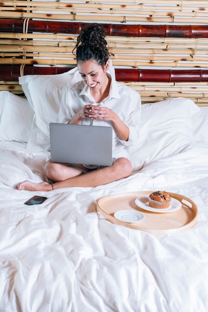 Mujer bonita con teléfono y computadora portátil en la cama