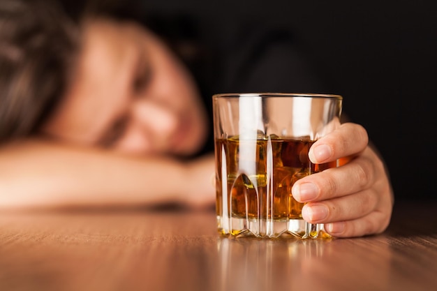 Mujer borracha durmiendo en el mostrador de bar sosteniendo un vaso de whisky