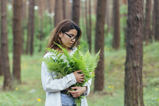 Una mujer en el bosque abraza un ramo de helechos, una joven activista protege el bosque