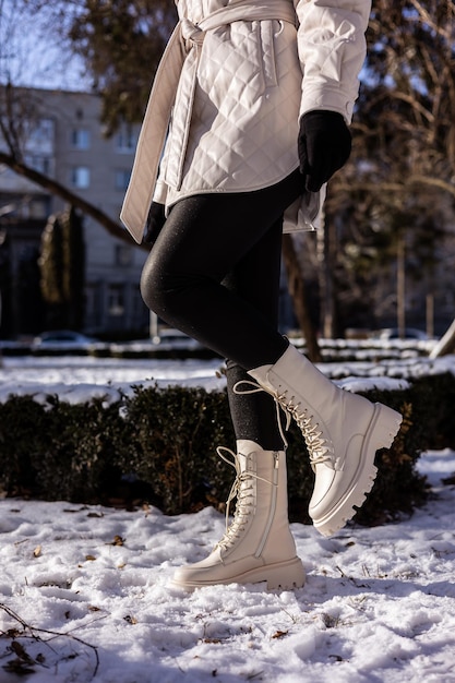 Mujer en botas blancas de moda en primer plano de nieve blanca