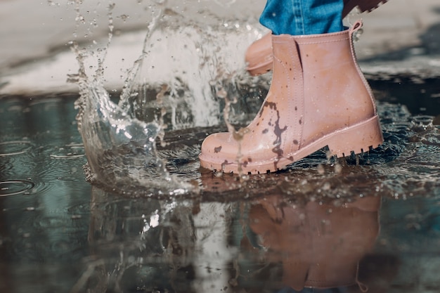 Mujer con botas de goma de lluvia caminando corriendo y saltando en un charco con salpicaduras de agua y gotas ...