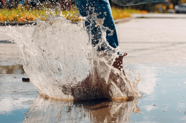 Foto mujer con botas de goma de lluvia caminar corriendo y saltando en un charco con salpicaduras de agua y gotas de lluvia de otoño.