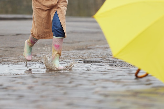 Mujer con botas de goma saltando sobre charco en primer plano de día lluvioso